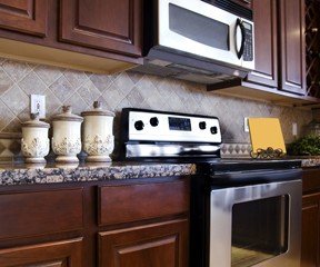 New Uses kitchen with dark-brown cabinetry, stainless steel appliances, neutral backsplash tile and cream-color canisters on multicolor countertop